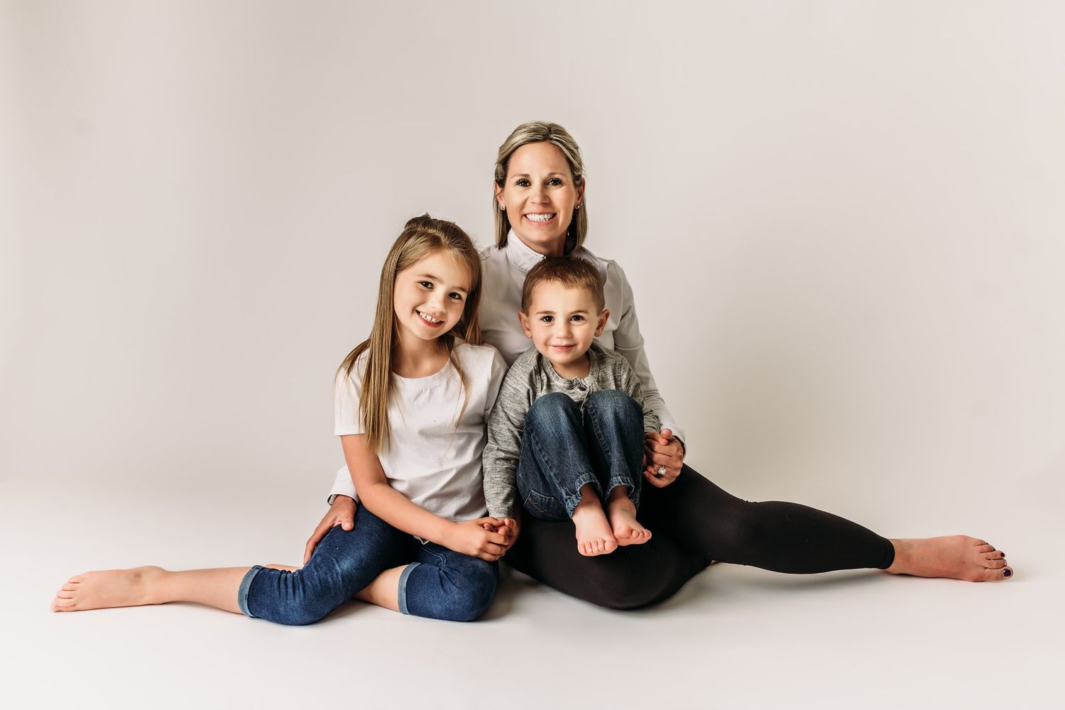 Family of three poses together on white studio backdrop in casual attire.