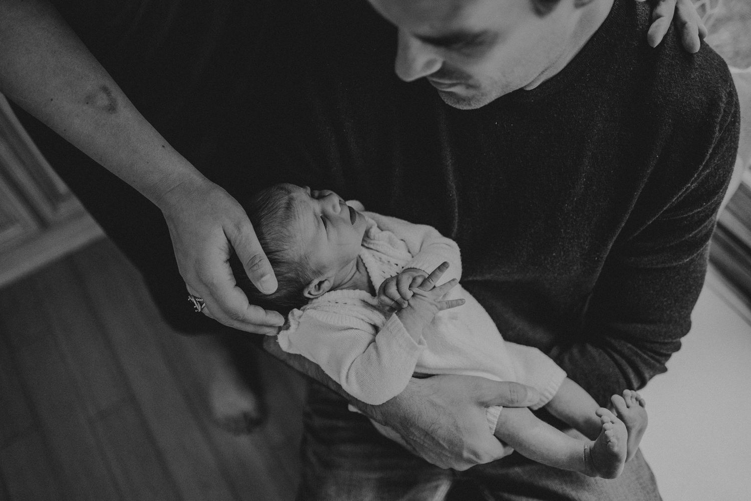Black and white image of tender moment between parent and infant in soft lighting.
