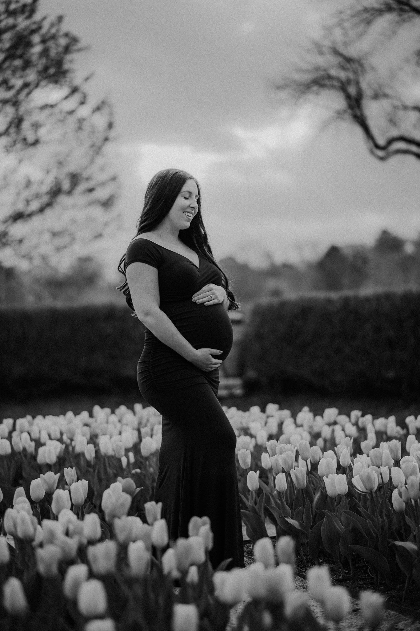 Black and white maternity portrait surrounded by blooming tulips in garden setting.
