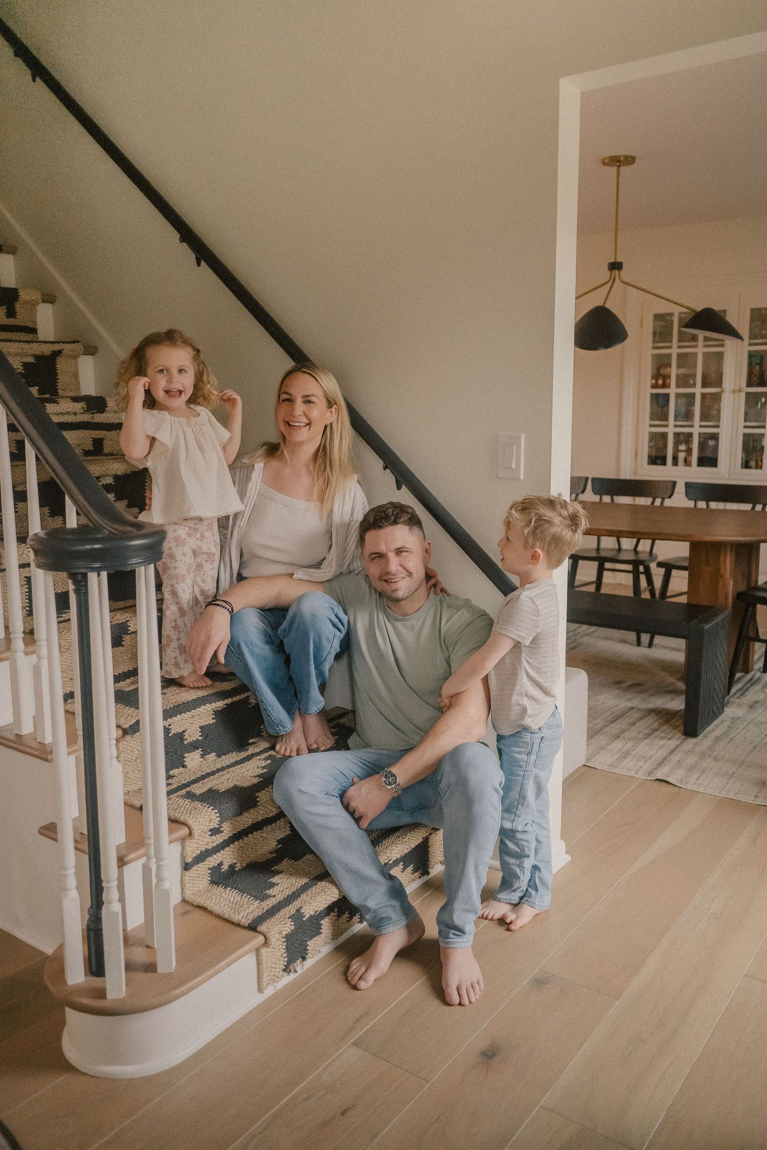 Happy family of four posing together on a staircase in a bright modern home interior.