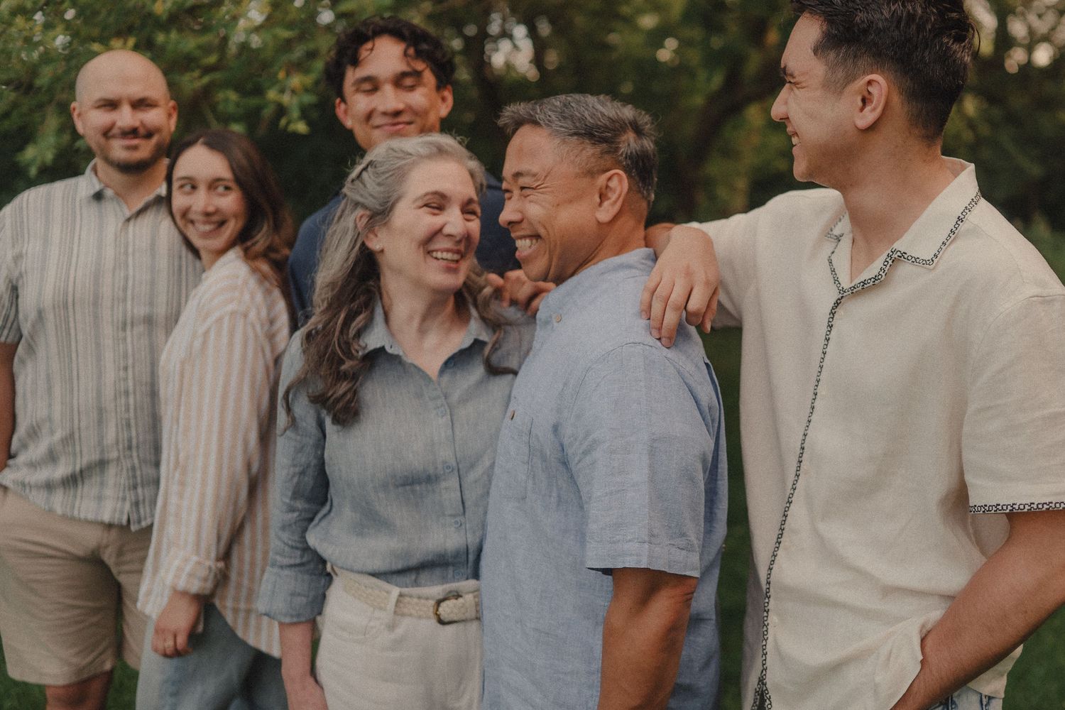 Multigenerational family laughing together outdoors in a park during a casual family portrait session.
