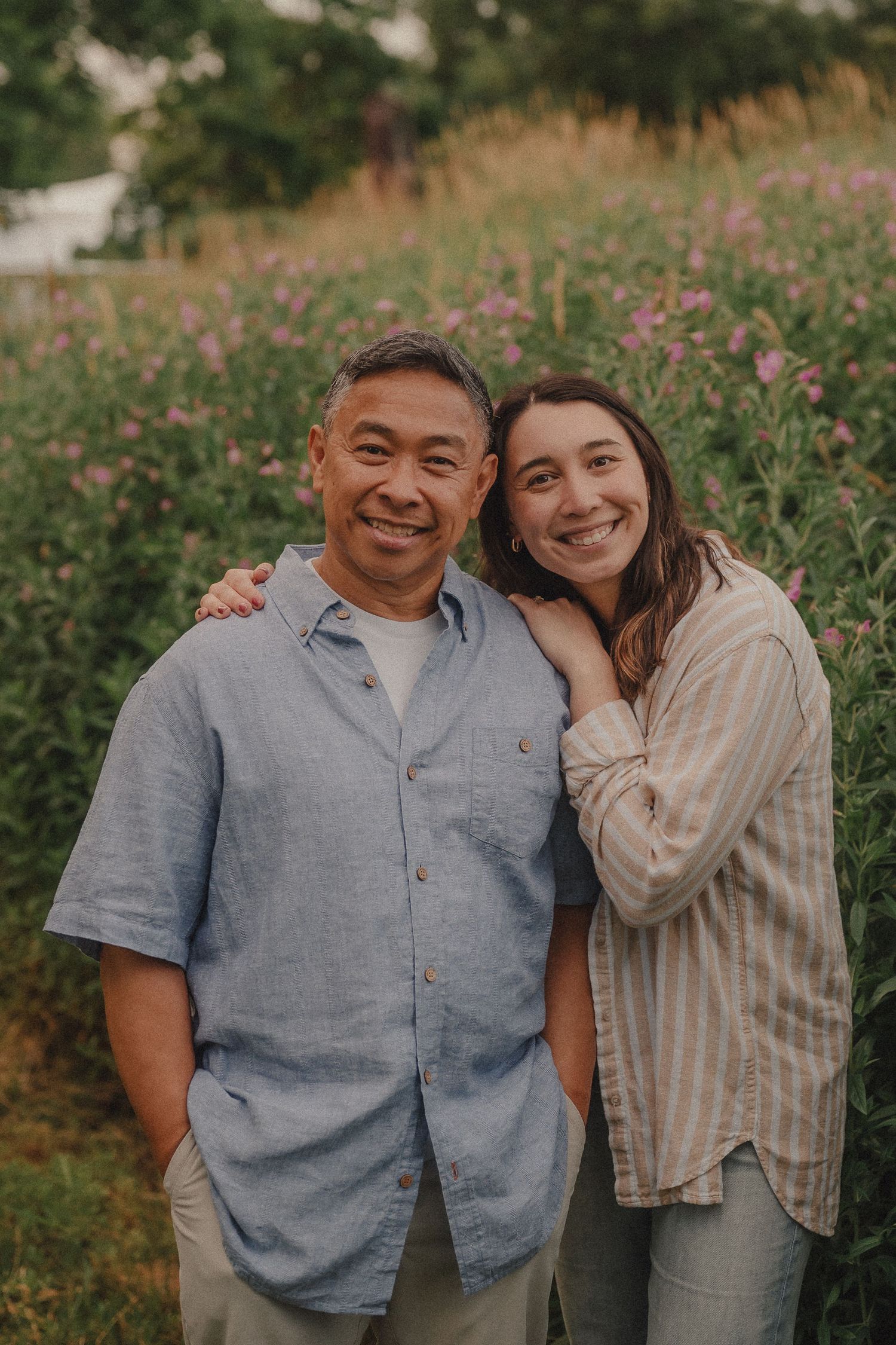 Smiling man and young woman posing together in front of a wildflower meadow.