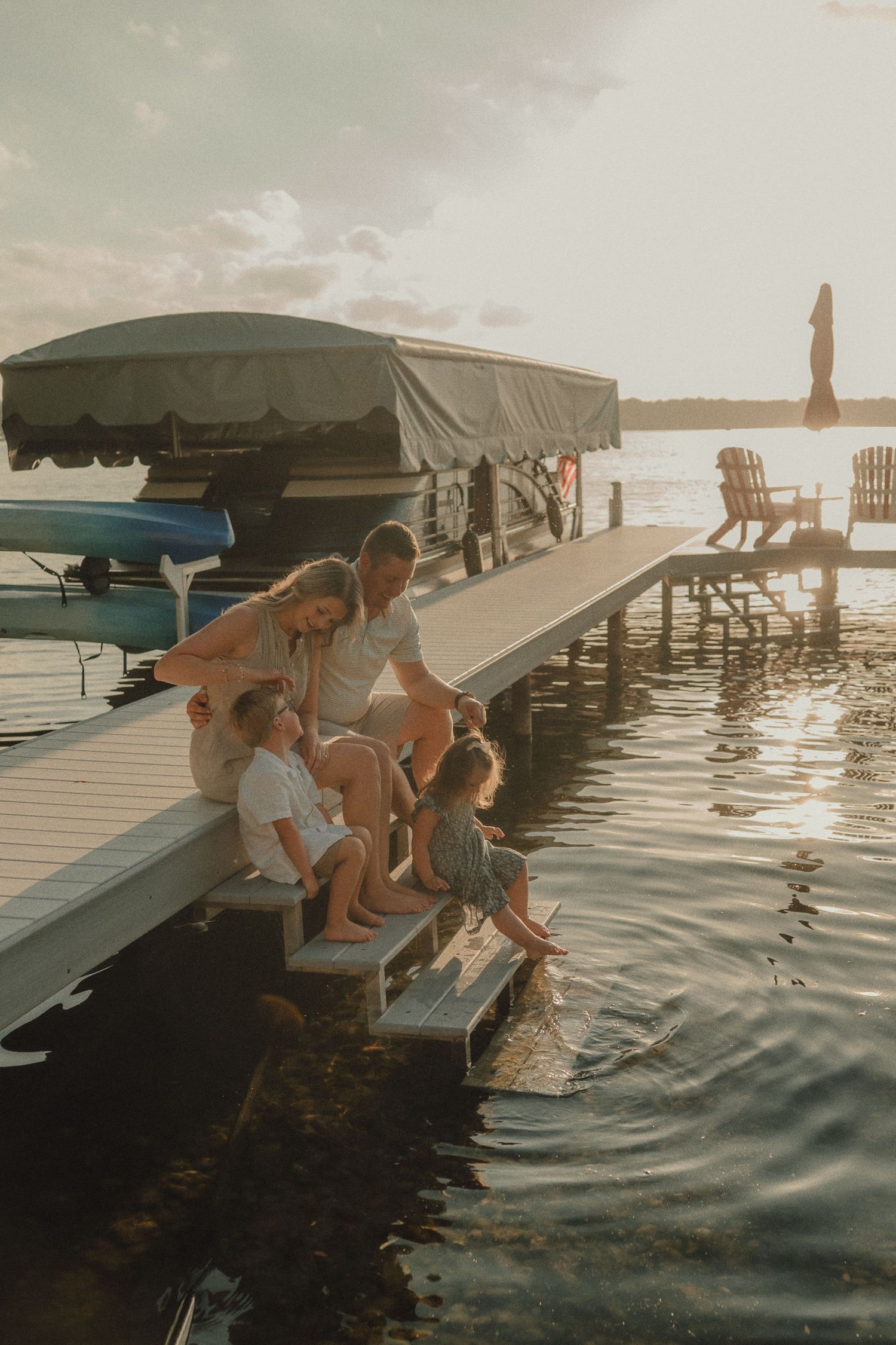 Family of four sitting together on a lake dock at sunset with feet in the water.