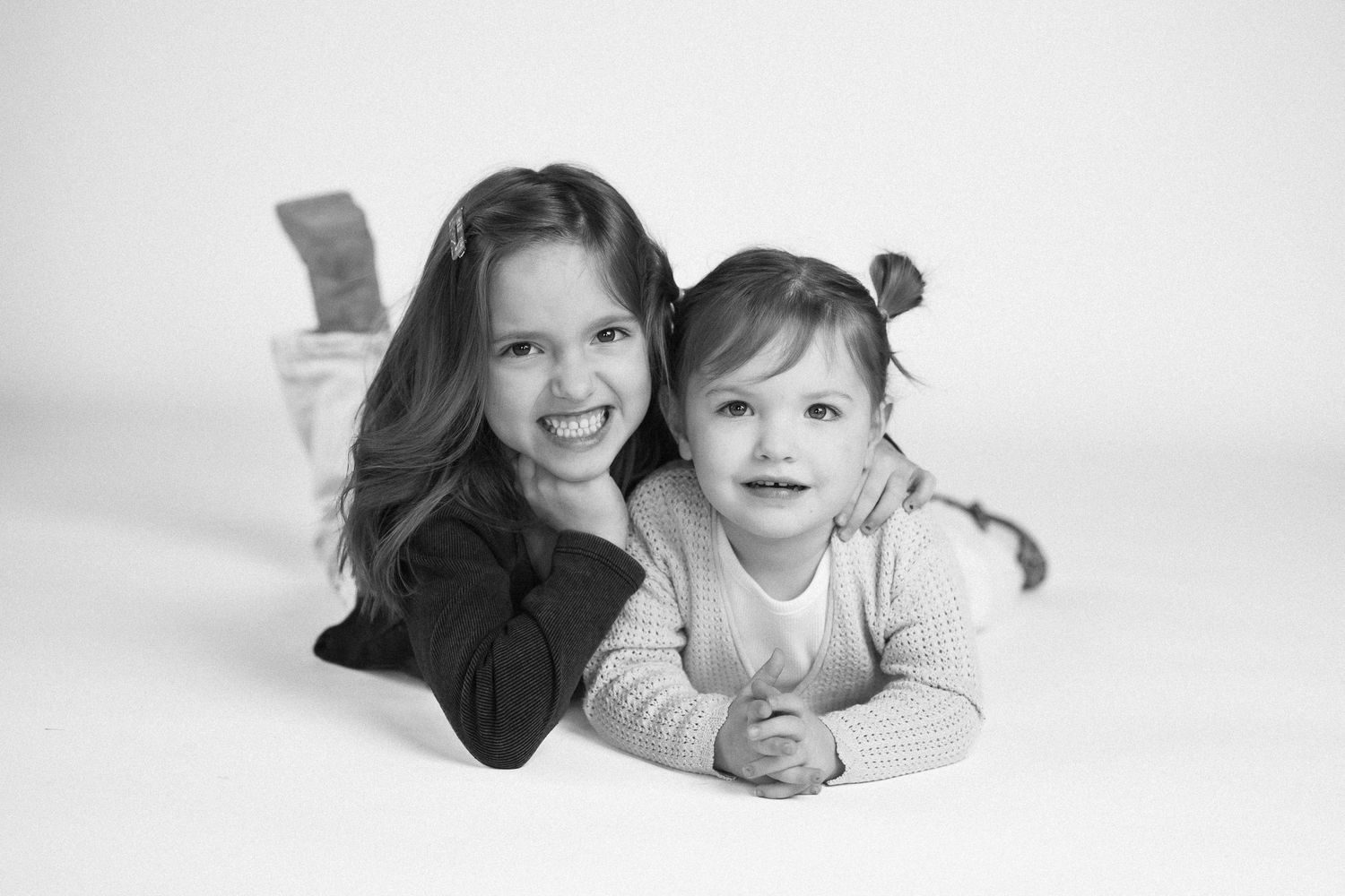 Black and white series of photos showing two people lying on the floor in playful poses against a white background.