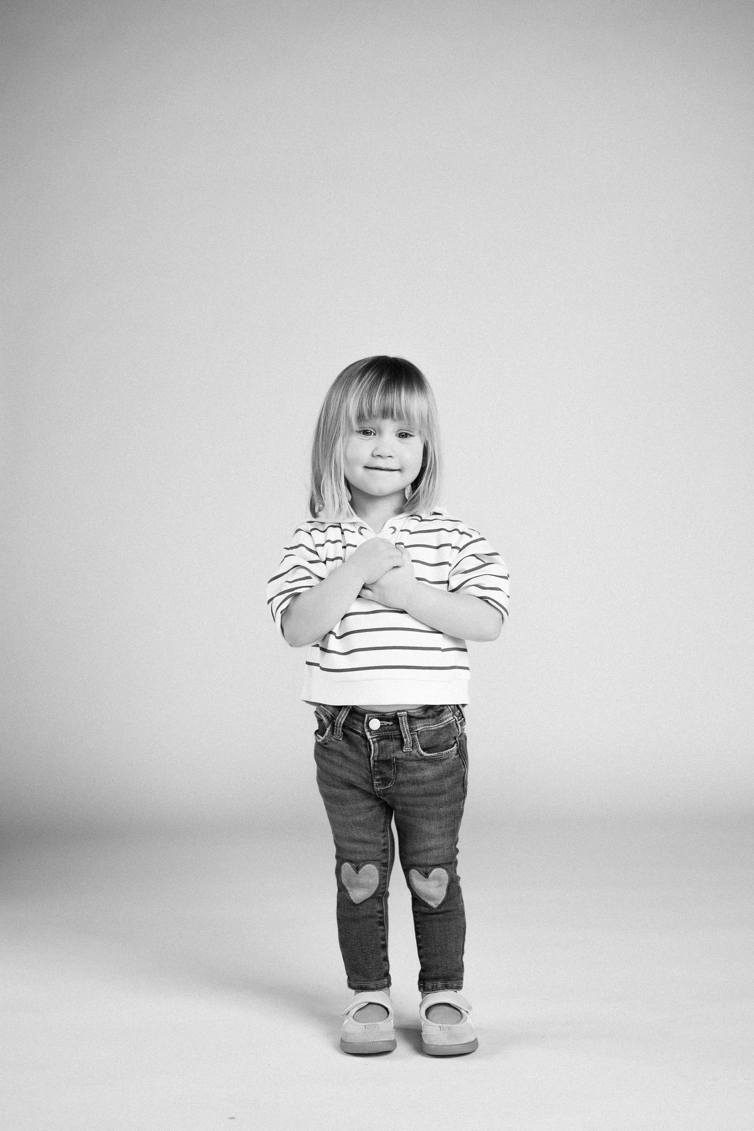 Black and white photo sequence of a toddler in striped shirt and jeans standing against white background.