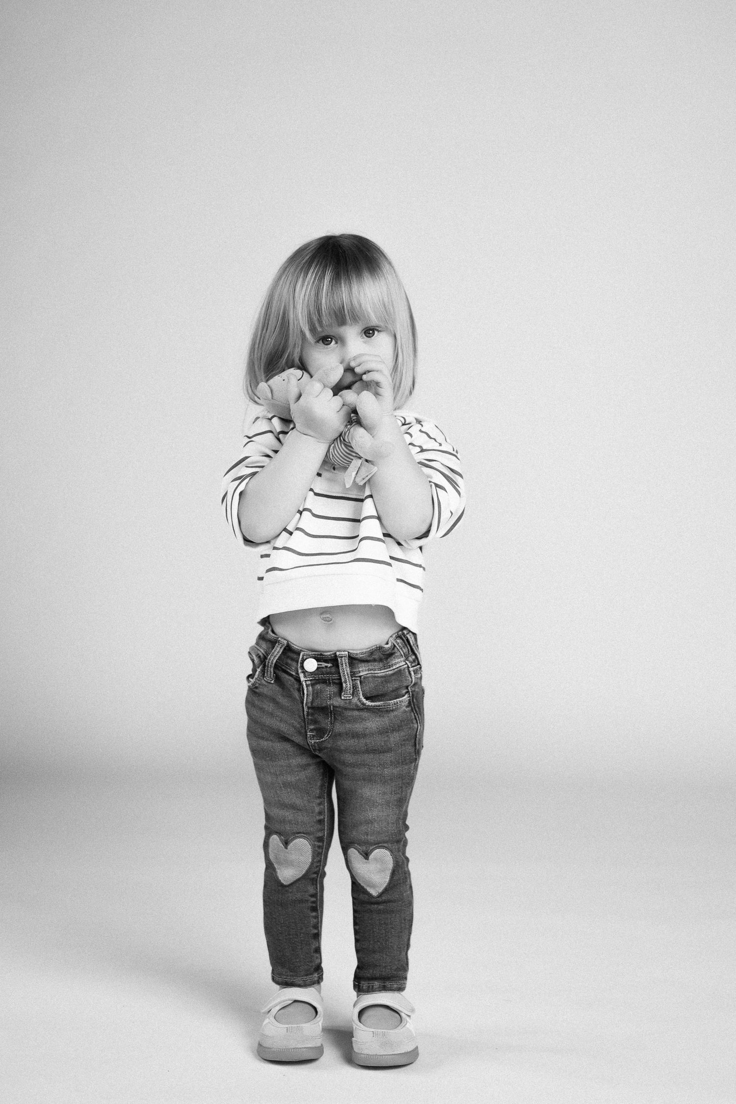 Black and white series showing a small child in jeans with heart patches playing peek-a-boo against white background.