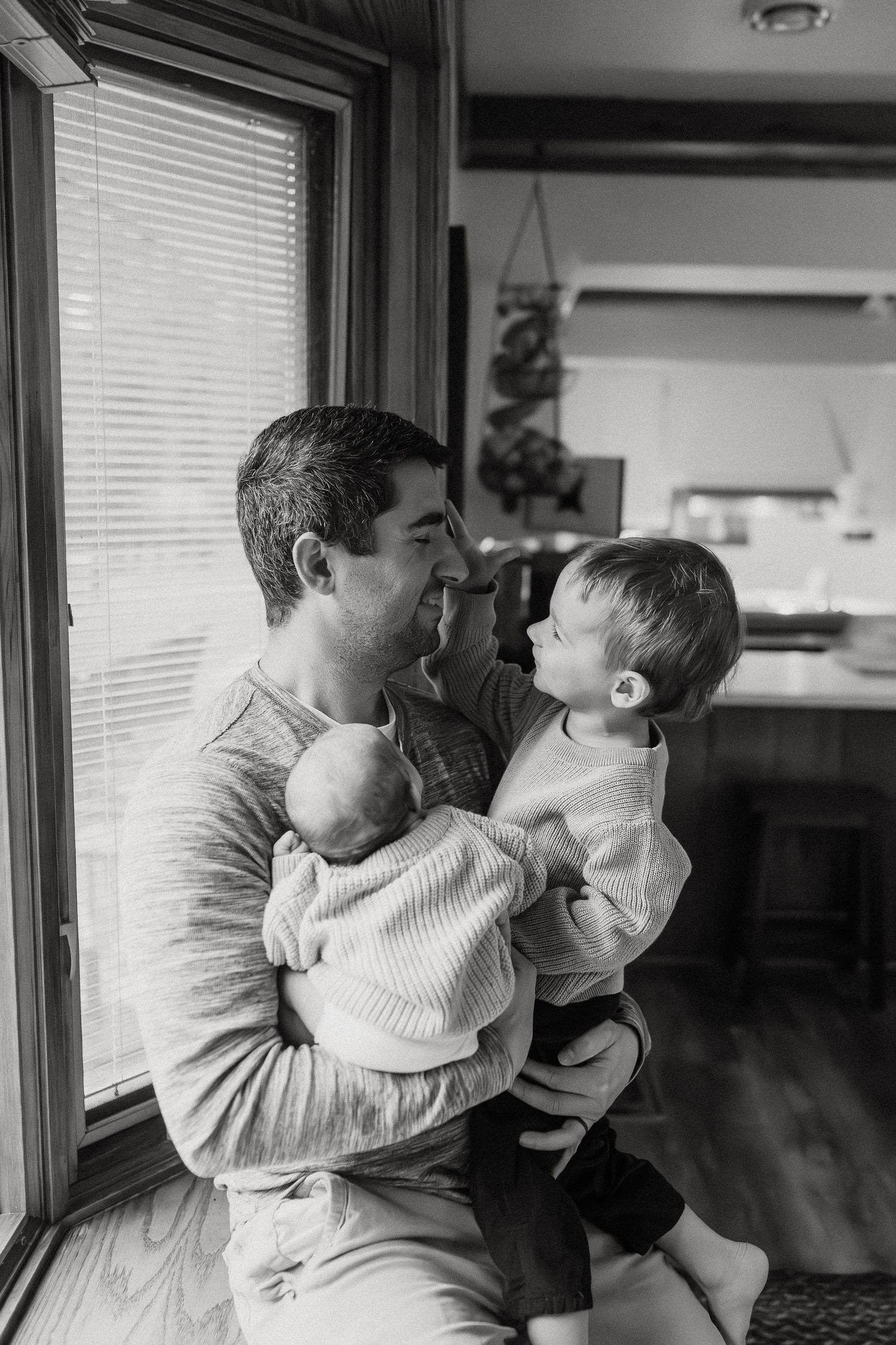 Black and white photo series showing gentle interactions near a window with natural light.