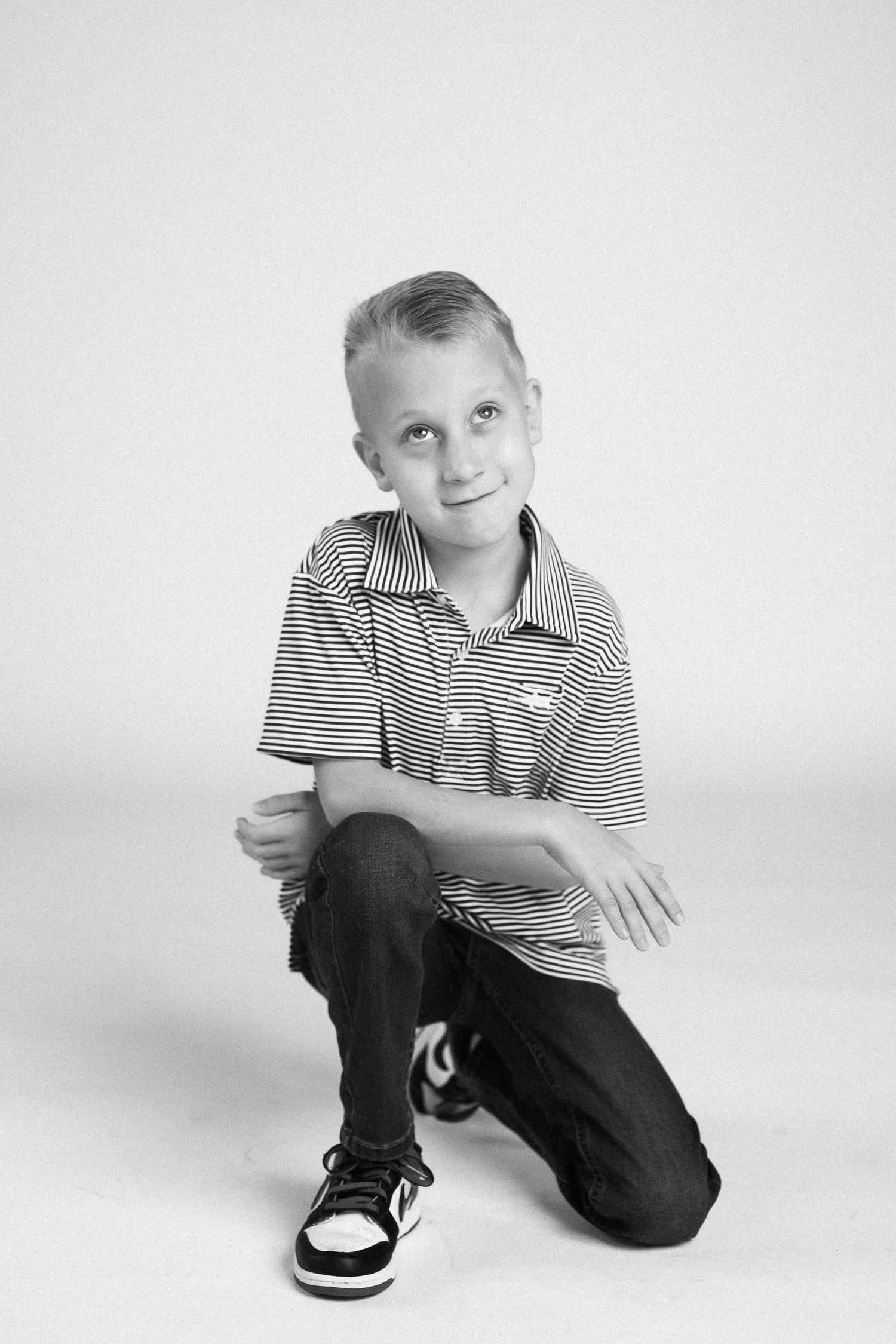 Black and white studio portraits of a young child in striped polo shirt and dark pants against white background.