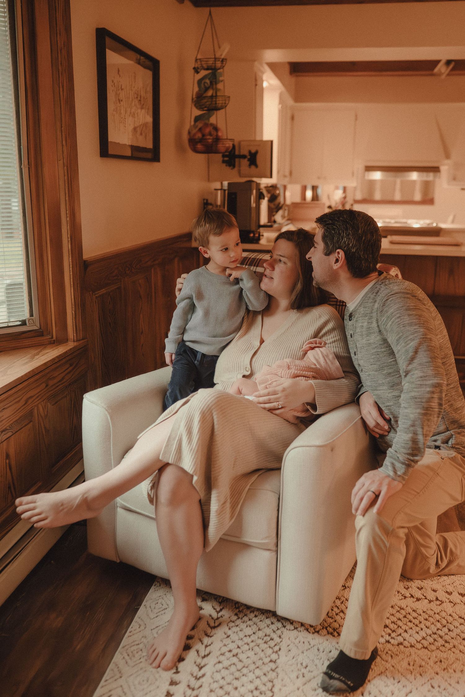 Family sharing tender moments together on a cream-colored couch in warm lighting.