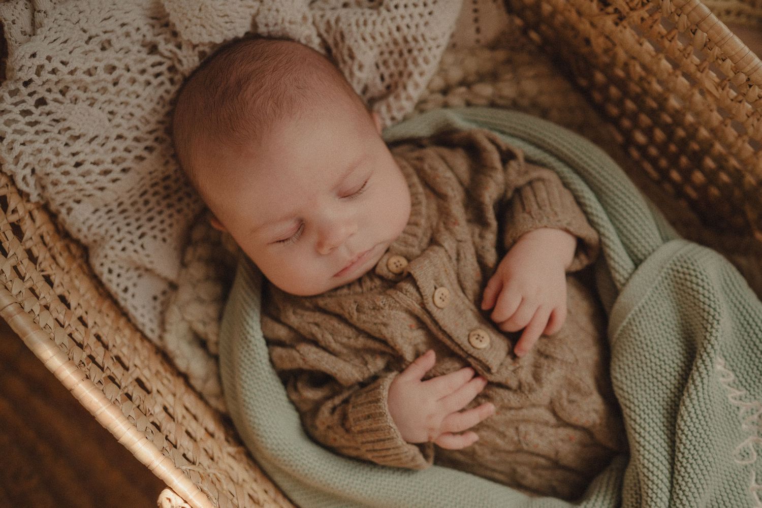 Sleeping baby wrapped in soft mint green blanket on textured knit surface.