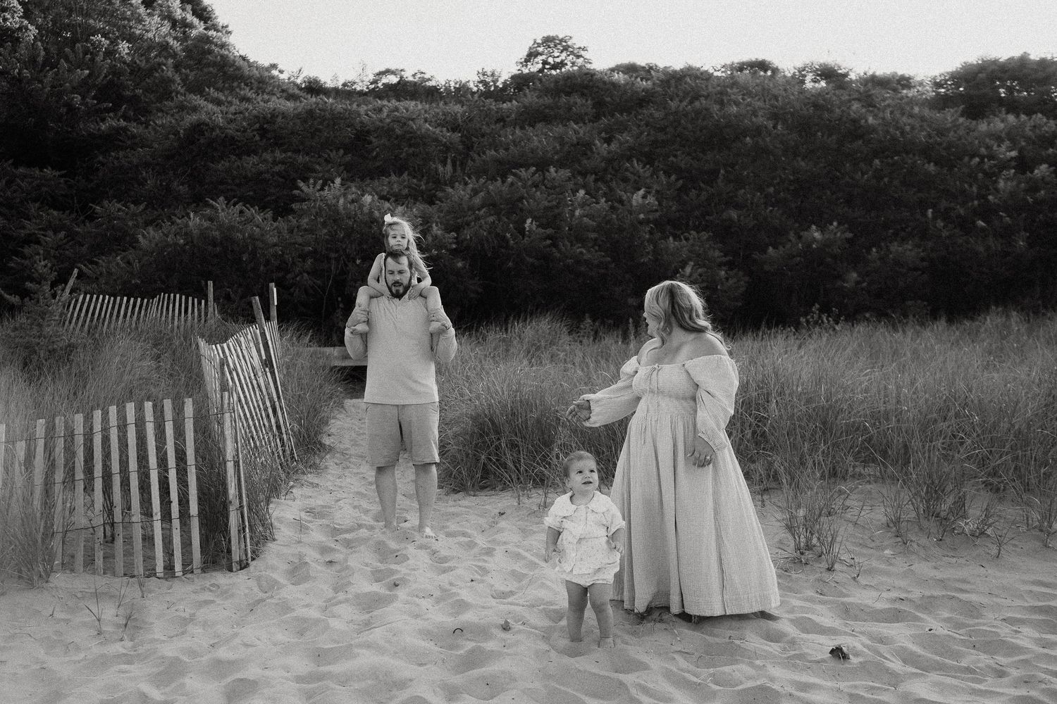 Black and white photo of family playing on sandy beach path.