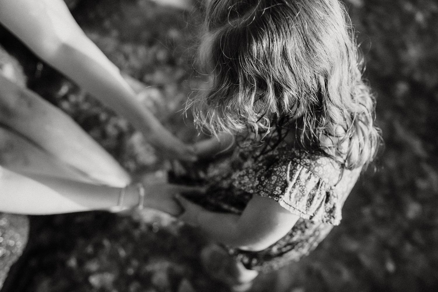 Black and white overhead photo of an adult holding hands with a young curly-haired child outdoors.
