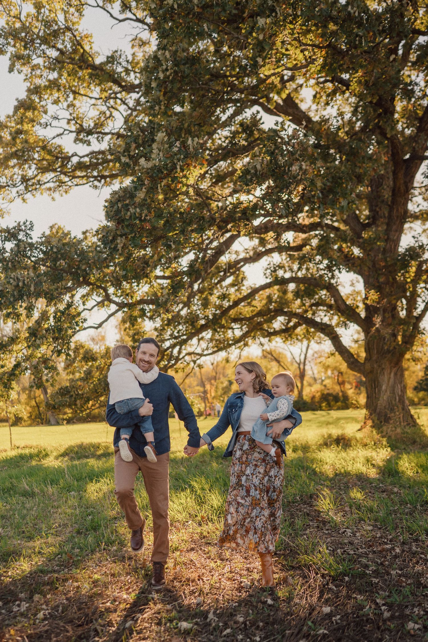 Family photoshoot under large oak trees during golden hour in a grassy field.