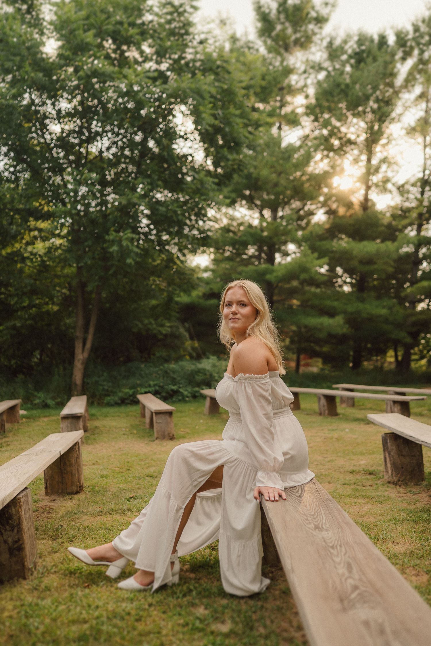 Person in white dress sitting on wooden benches in a park setting.