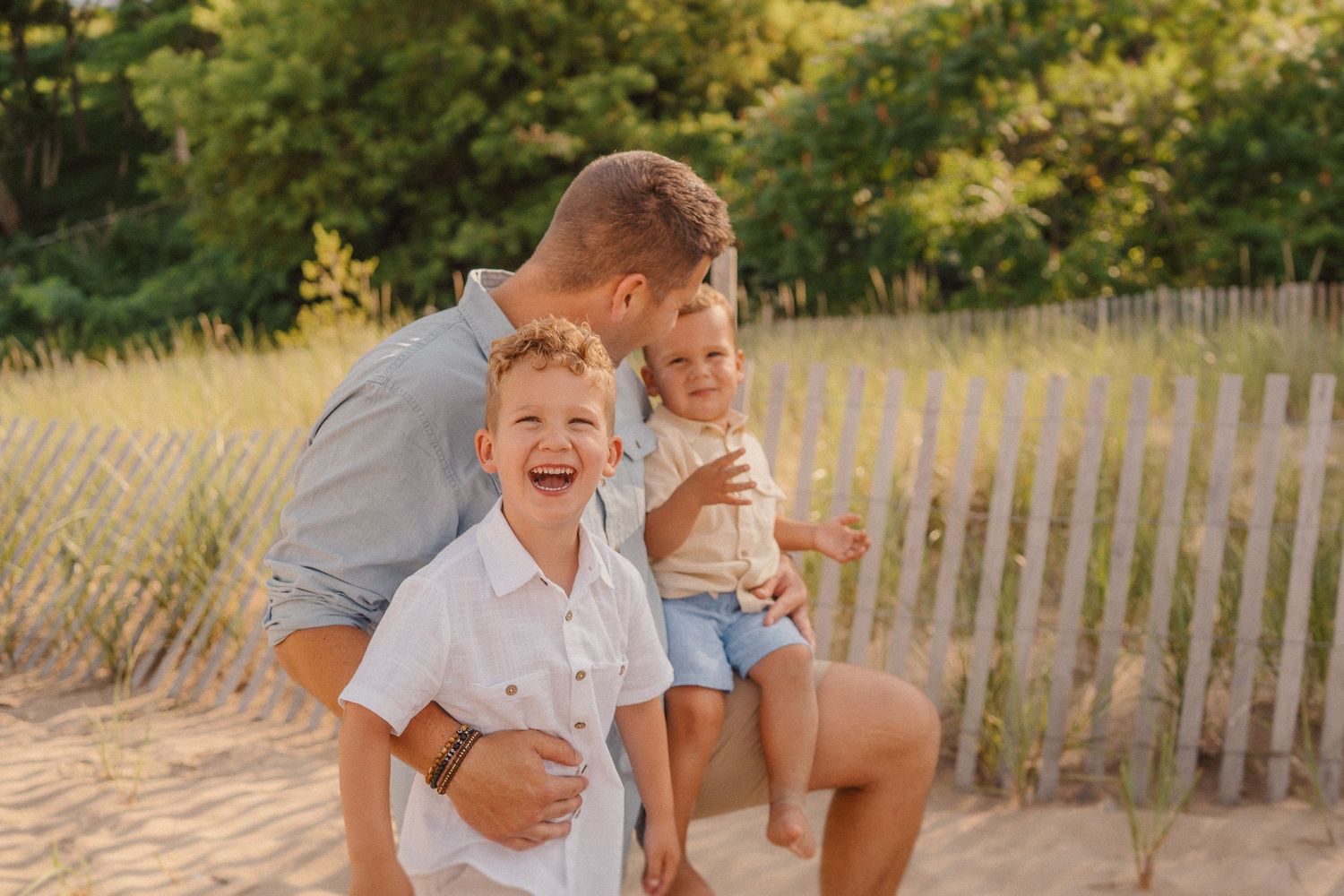 Candid family moment shared on beach with wooden fence in background.