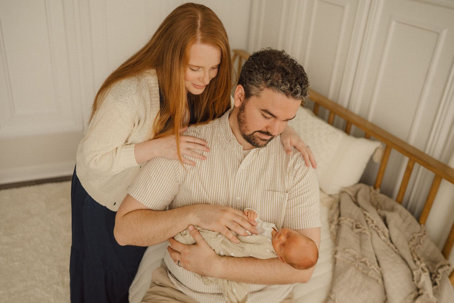 A couple shares an intimate moment caring for their newborn baby in a serene bedroom setting.