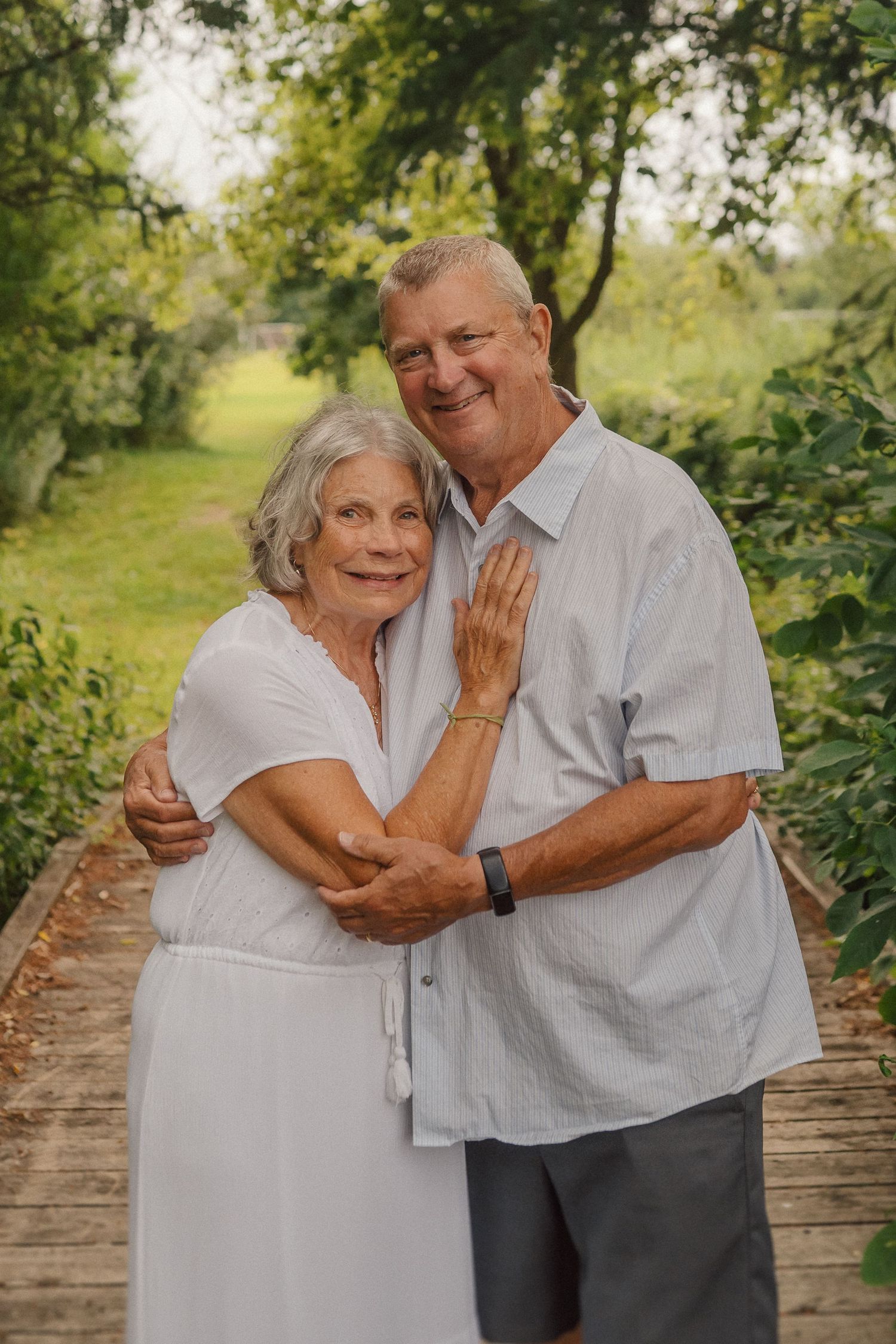 Senior couple shares affectionate moment while standing together on wooden bridge path.
