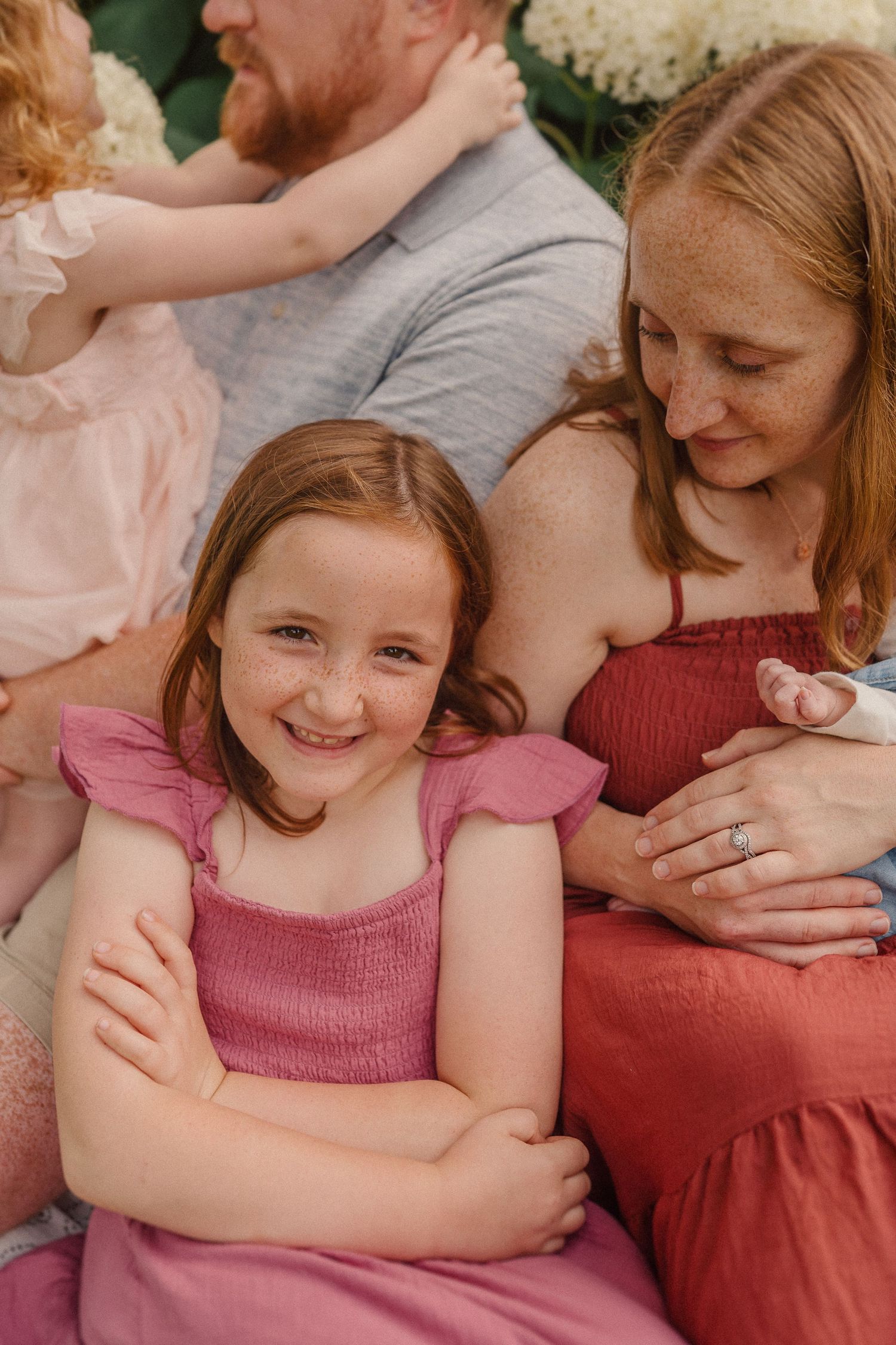 Family gathering outdoors wearing pink and red dresses with soft natural lighting creating intimate atmosphere.