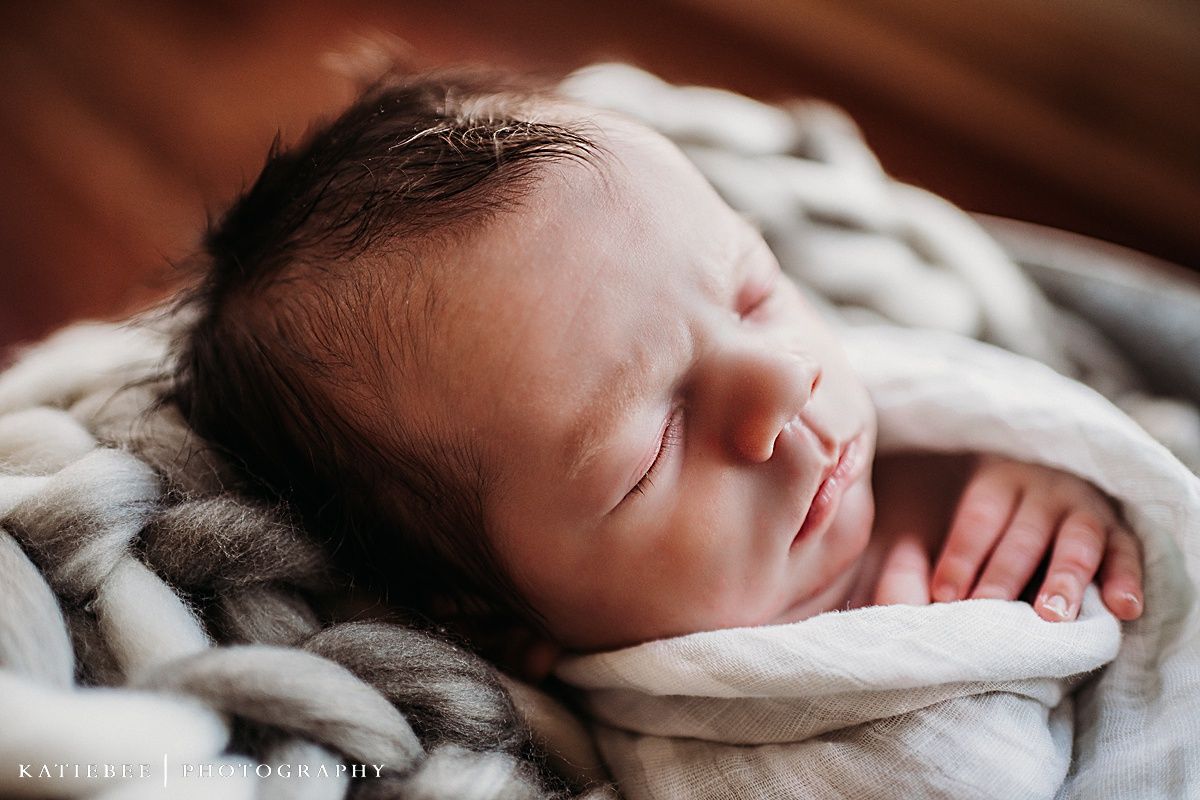 Peaceful sleeping newborn wrapped in cozy knit blanket during photo session.
