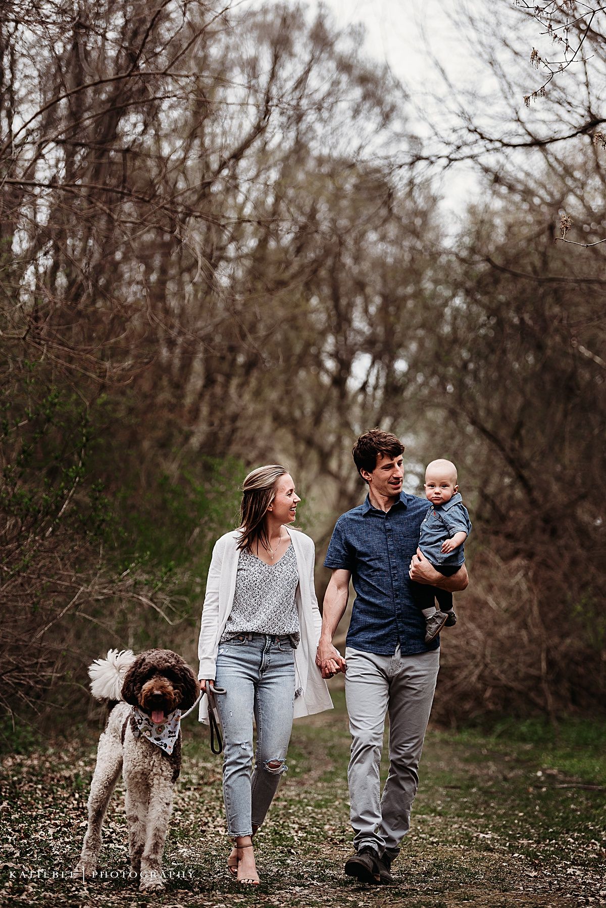 Family walking on forest trail with their spotted dog on sunny day.
