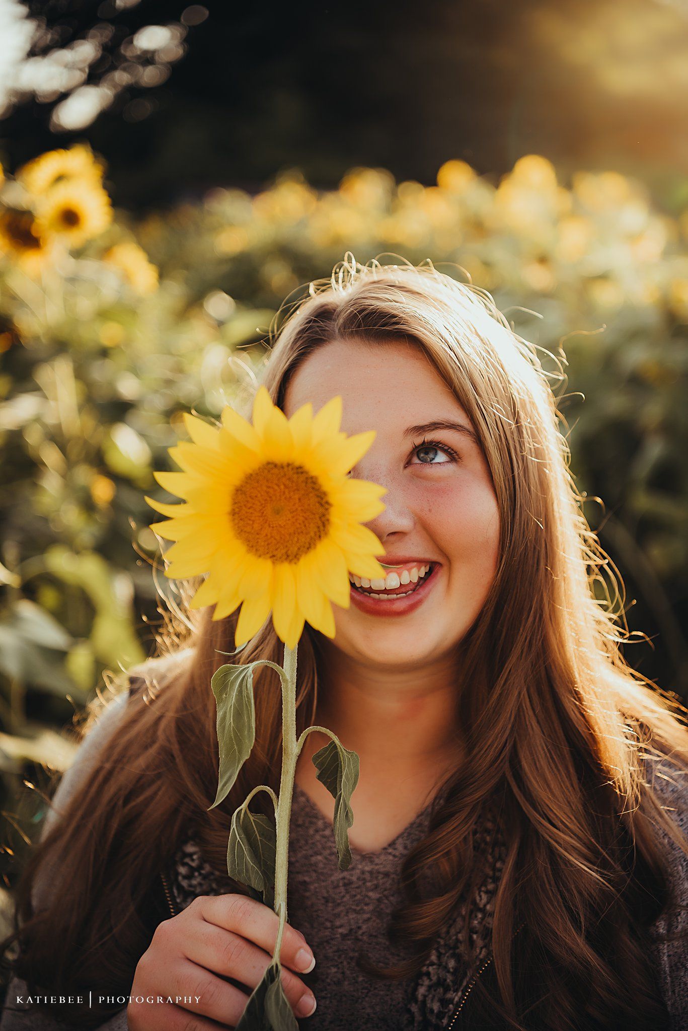 Playful outdoor portrait with a bright yellow sunflower and warm backlit glow.