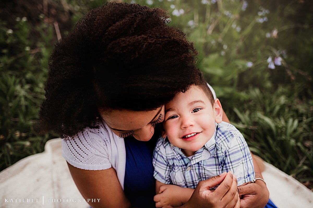Intimate close-up portrait amidst greenery showing affectionate family moment.