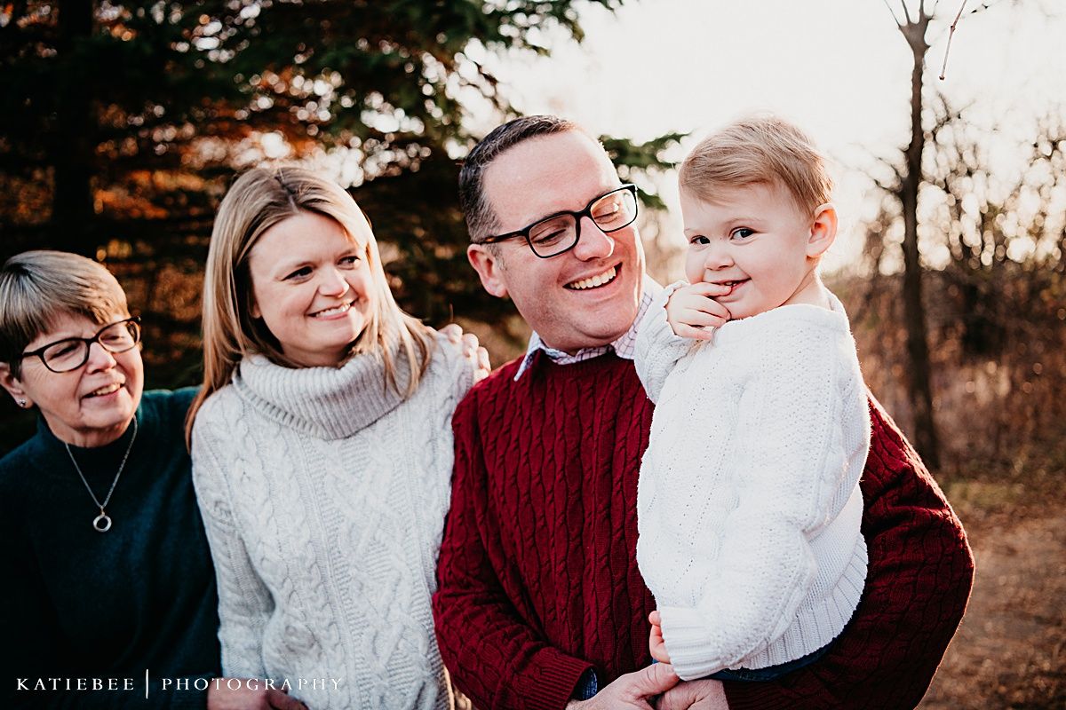 Family portrait captured outdoors at sunset showing warm smiles and coordinated burgundy and white sweaters.
