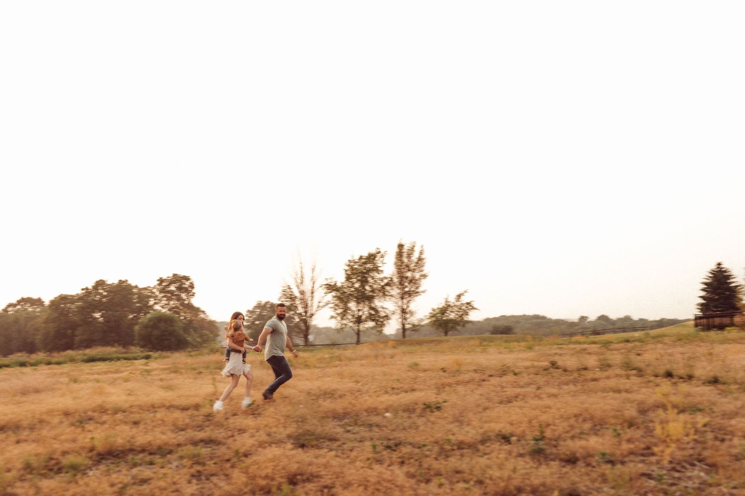 Two people run playfully through a sunlit field at dusk.