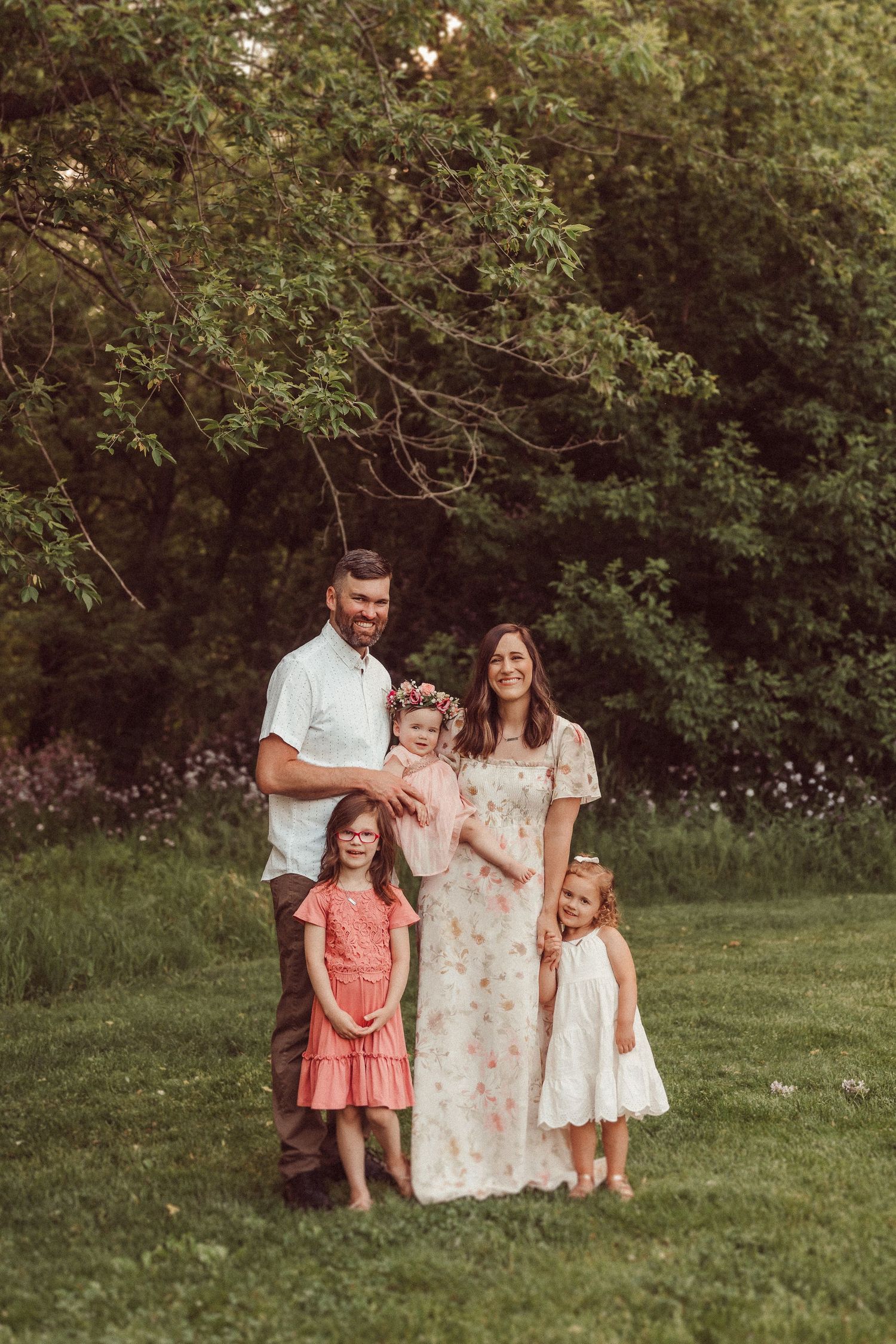 Family of five posing together in a lush green field during summer.
