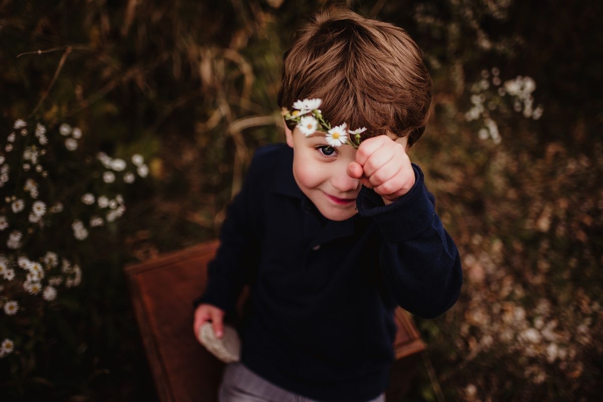 Child wearing glasses rubs eye while sitting on wooden surface outdoors.
