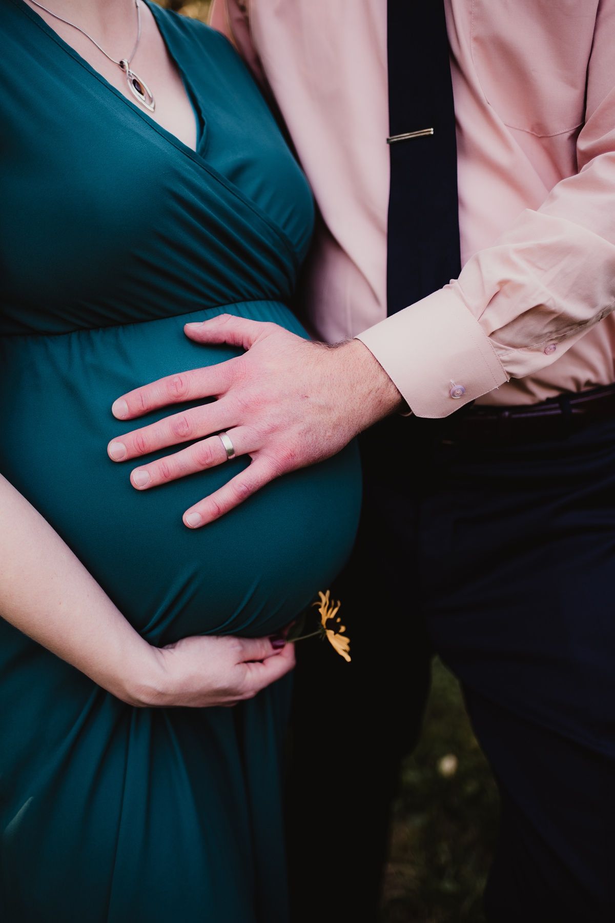 Close-up of couple's hands on pregnant belly, wearing teal dress and pink shirt.