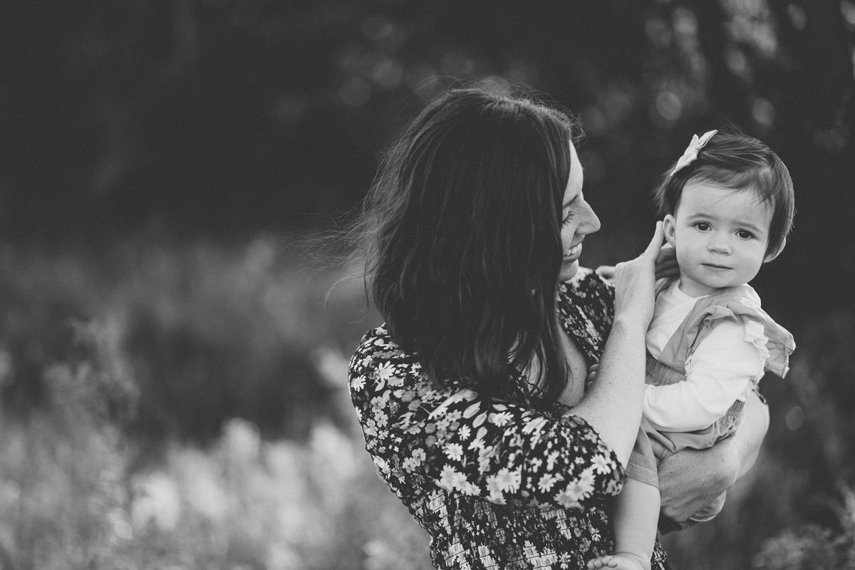 Black and white portrait showing tender moment between adult and baby in natural setting.