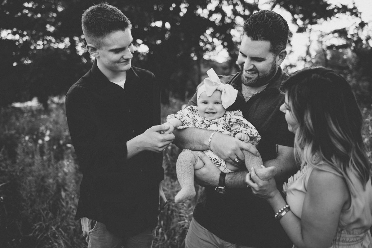 A family shares a tender moment outdoors with their baby in black and white photography.