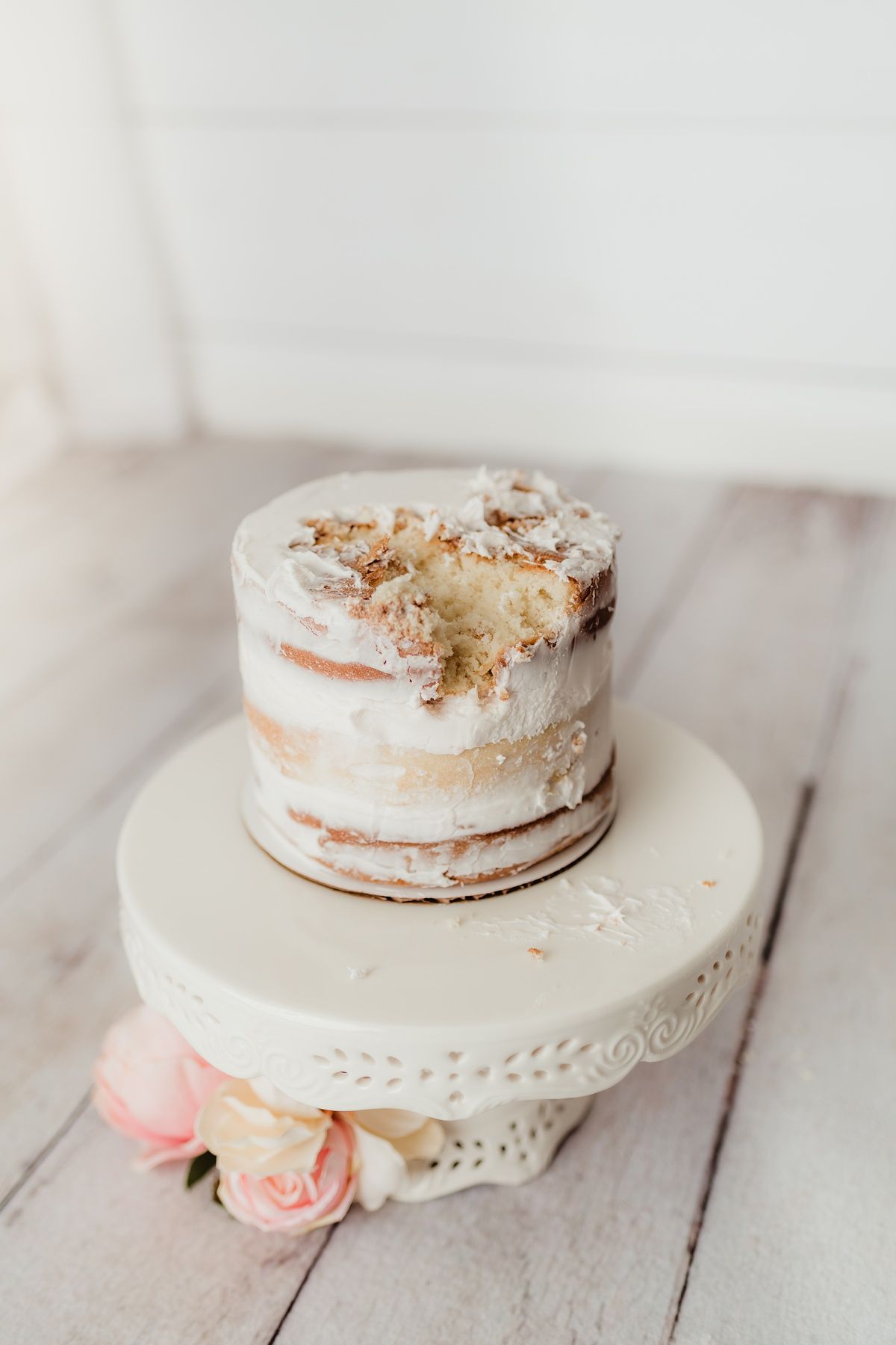Semi-naked white cake with fresh flowers on vintage cake stand against white background.