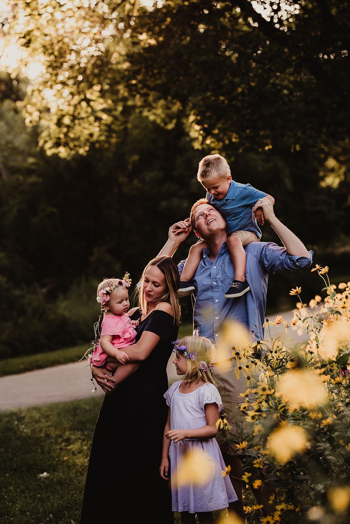 A playful family portrait at sunset with golden bokeh lights from flowers in the foreground.
