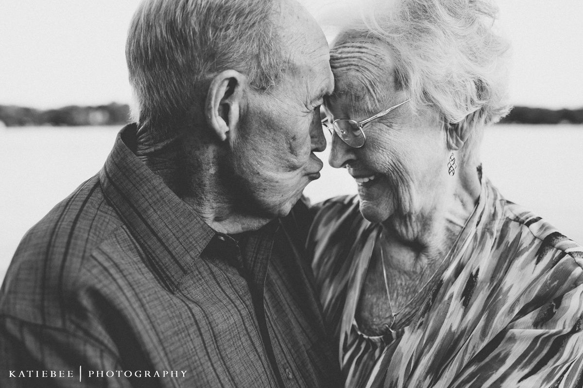 An elderly couple share an intimate moment in black and white photography.