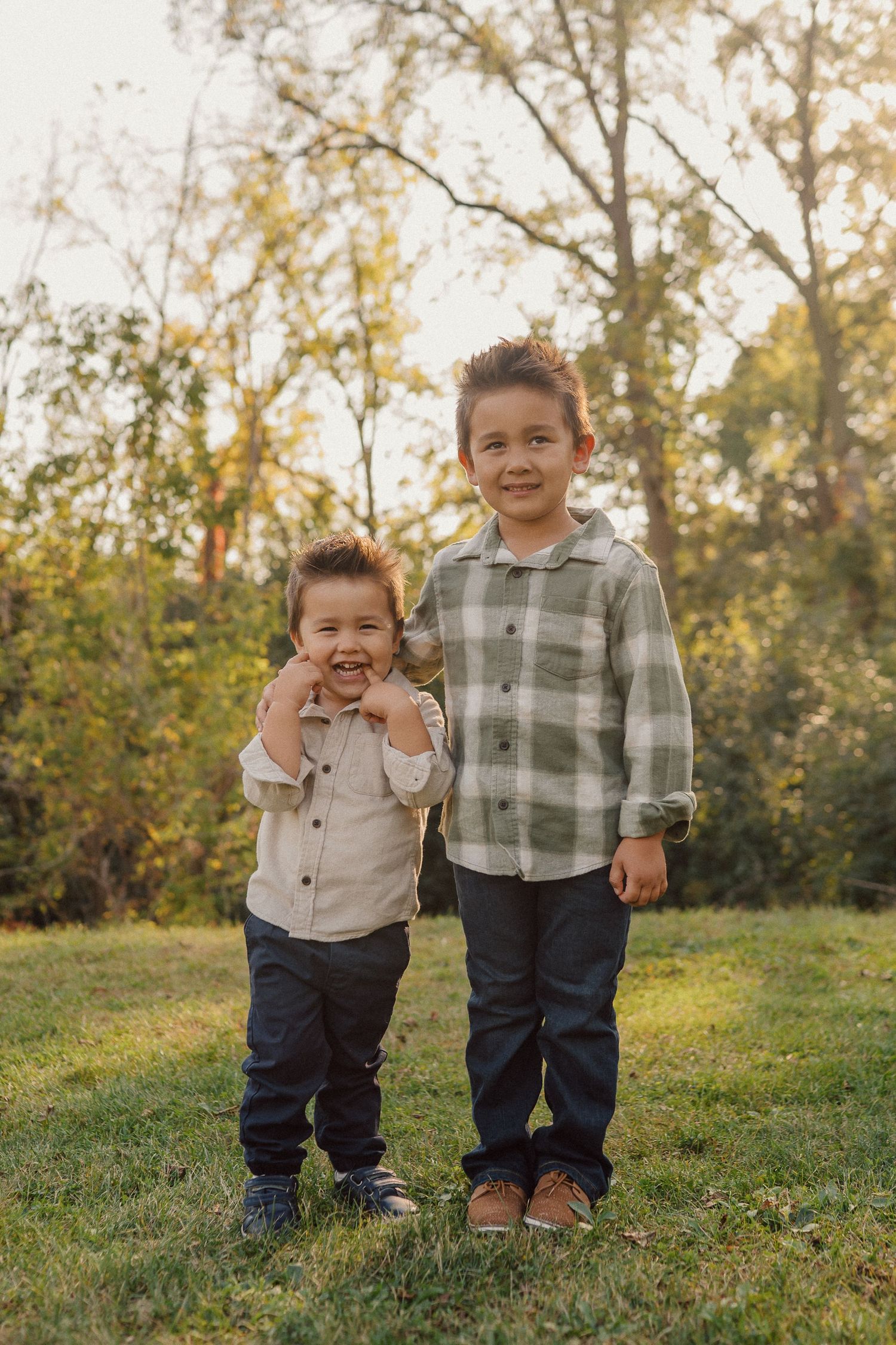 Two young children in casual attire stand together on a grassy hill during golden hour.