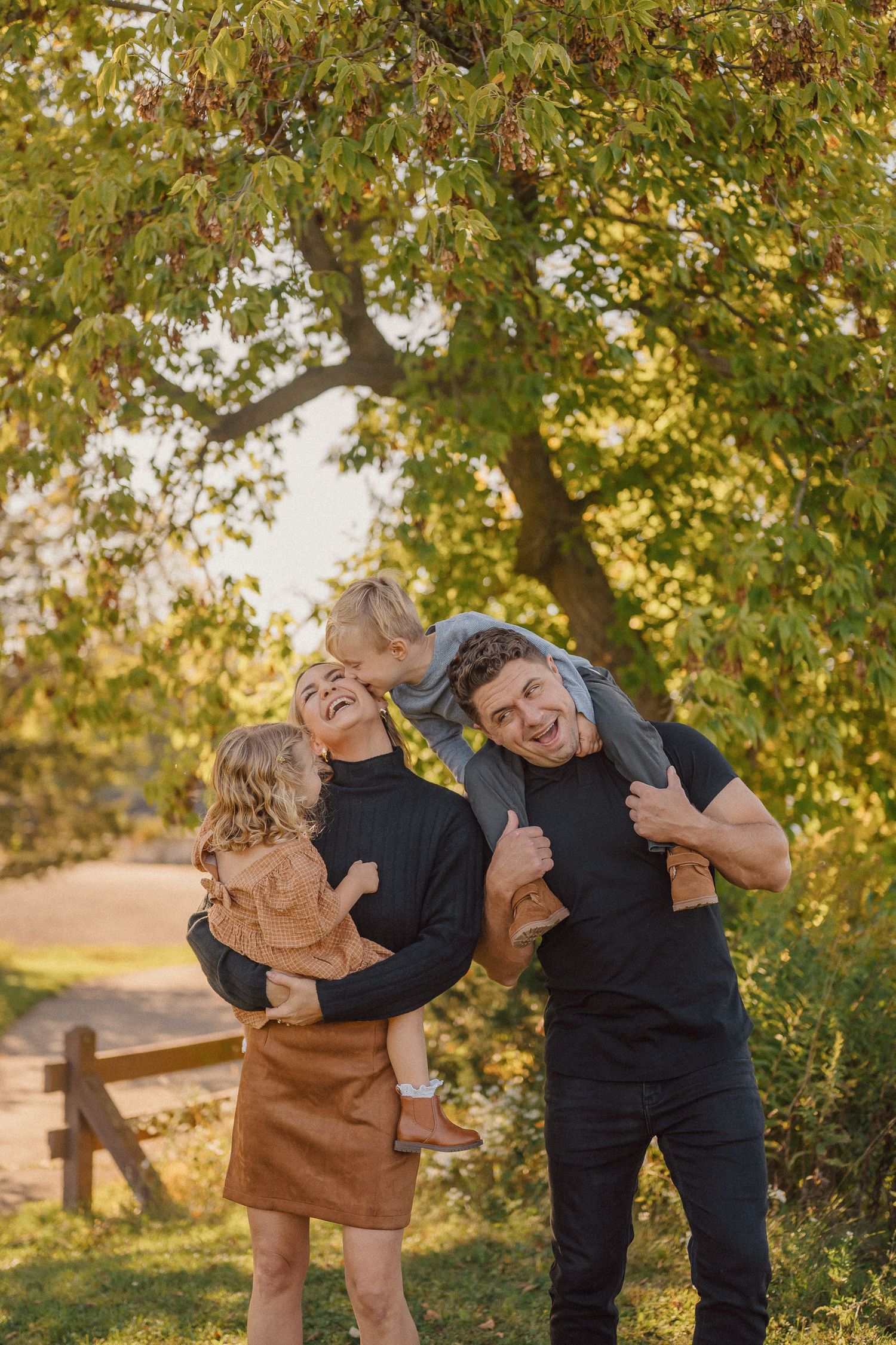 Playful outdoor family photoshoot with joyful expressions under autumn trees.