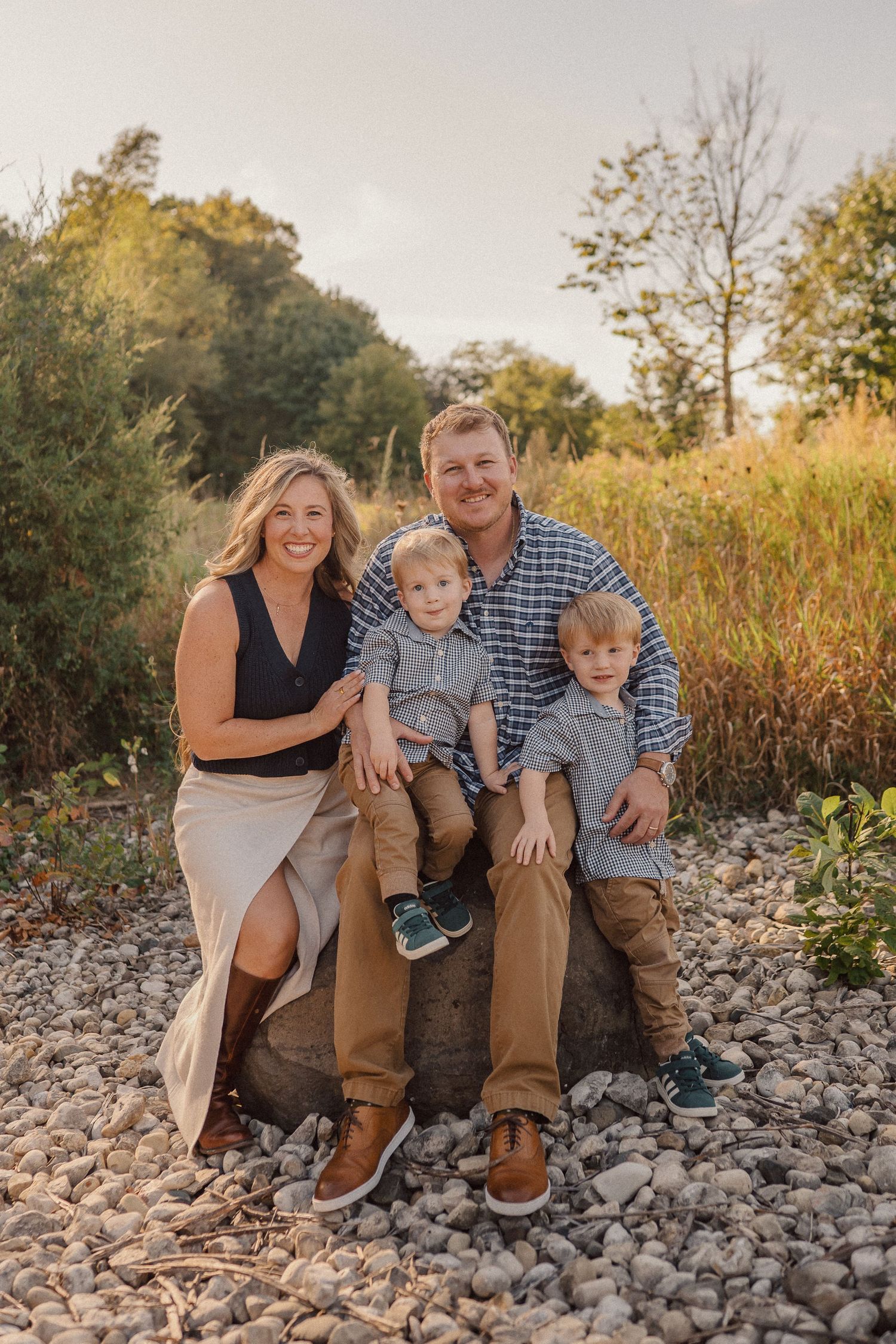 Candid family portrait captured on rocky ground with natural autumn scenery in the background.