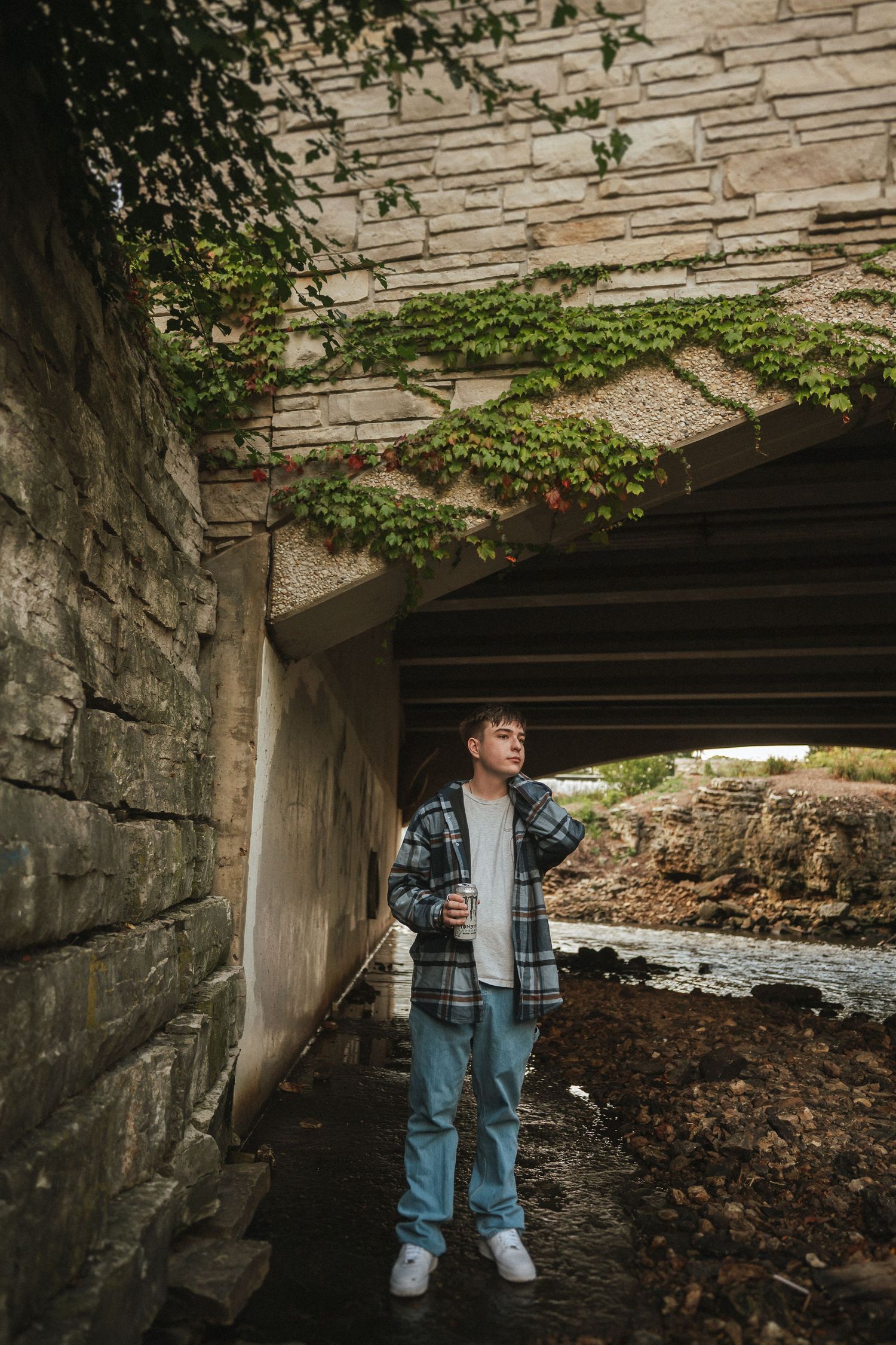 A person wearing a denim jacket stands under a stone bridge structure surrounded by fallen leaves.
