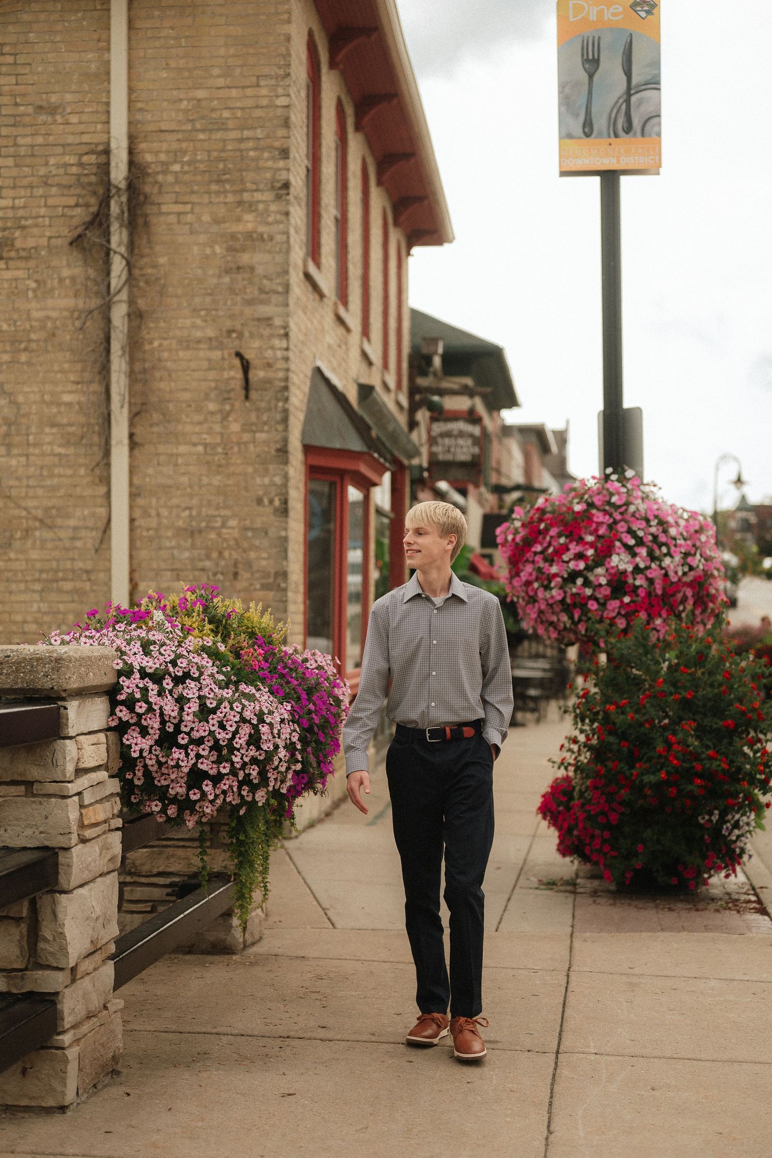 A person walking past vibrant hanging flower baskets along a brick building sidewalk.