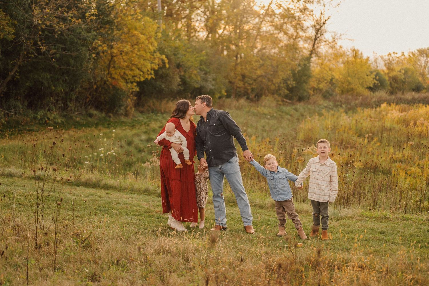 Family walking through golden meadow at sunset with natural fall scenery in background.