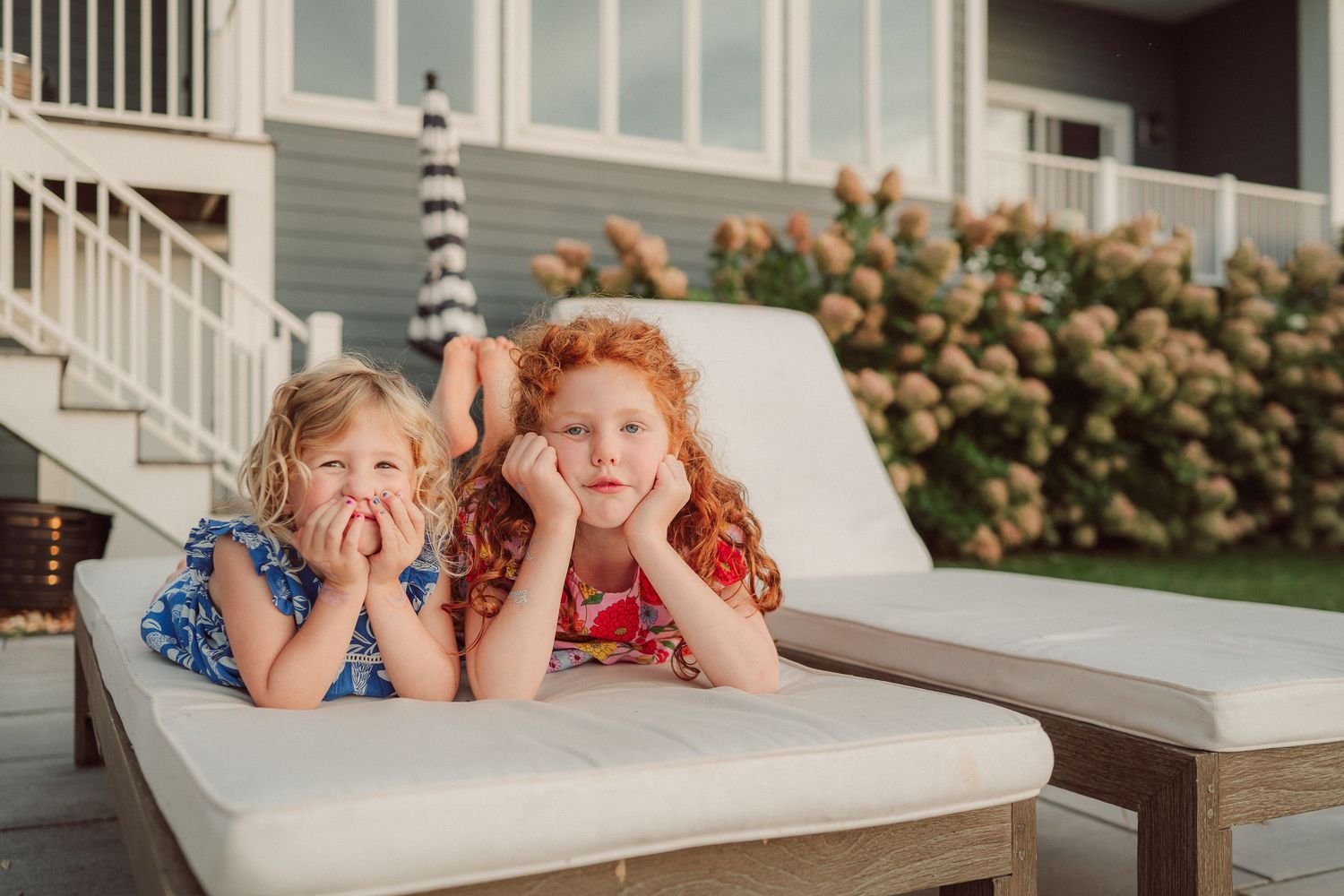 Two children make silly faces while lounging on an outdoor patio chair together.