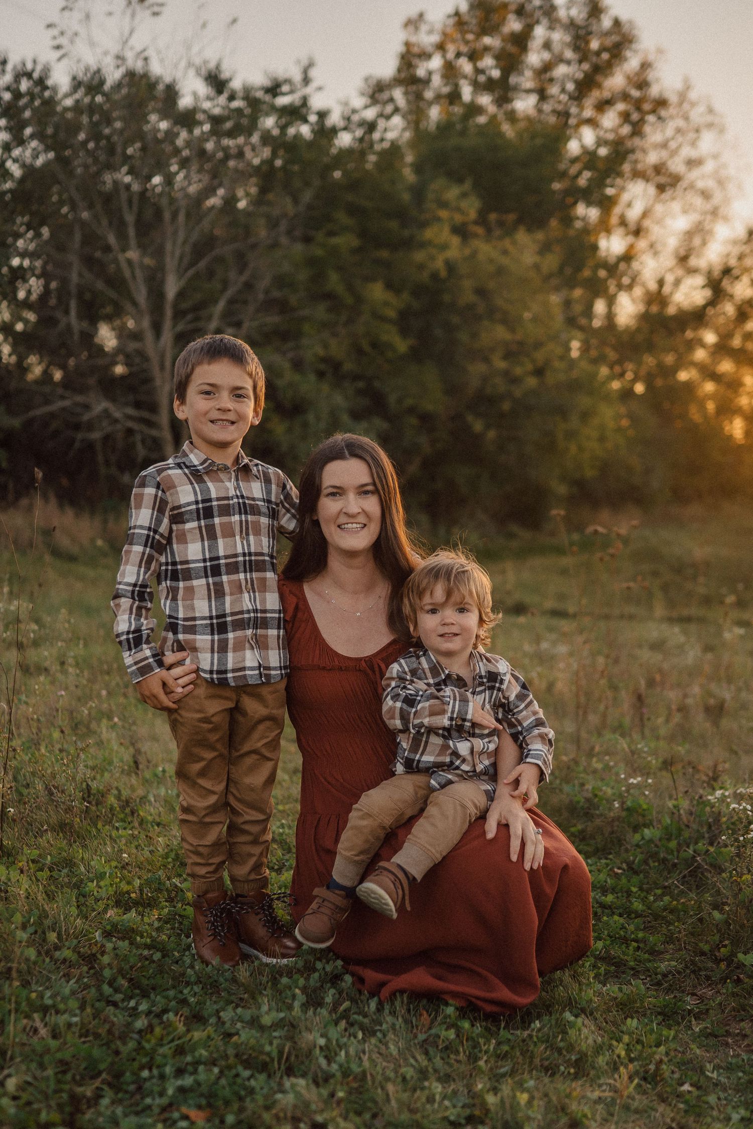 A family poses together in a field at sunset wearing coordinating burgundy and plaid outfits.