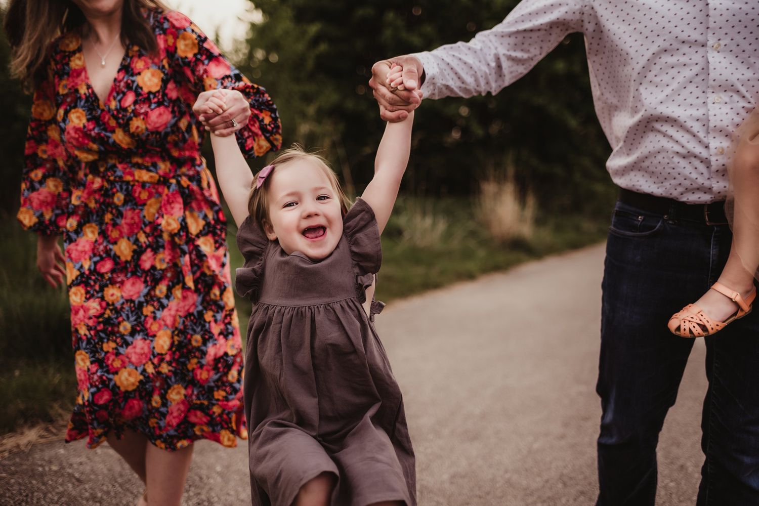 Joy radiates as a child in brown clothing swings between two adults on a path.