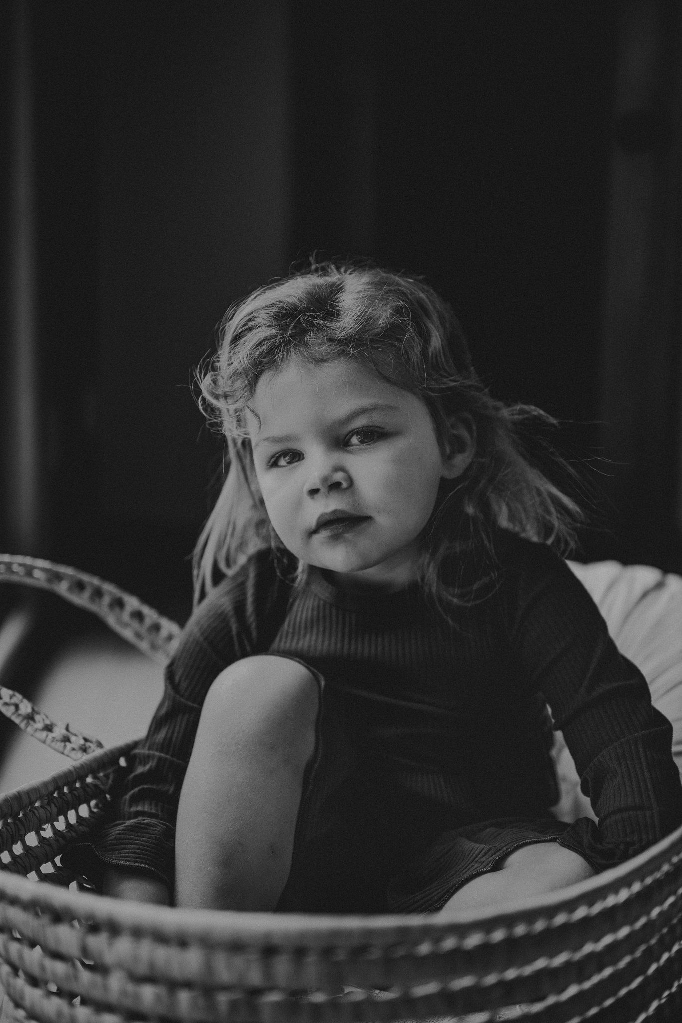 Dramatic black and white portrait of child sitting in woven basket.