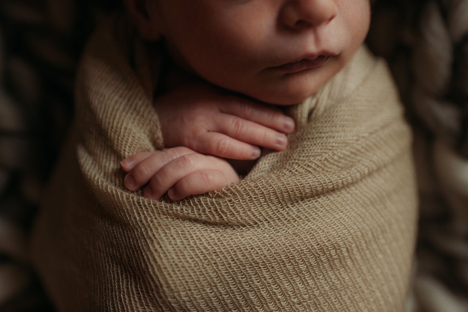 Close-up of newborn baby wrapped snugly in neutral colored swaddle.