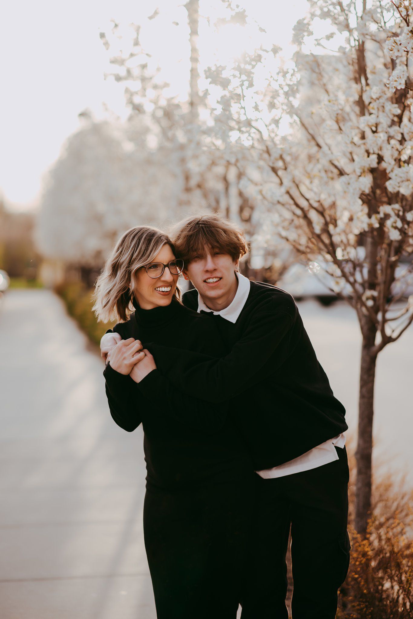 Couple in black sweaters sharing tender moment outdoors near blooming trees.
