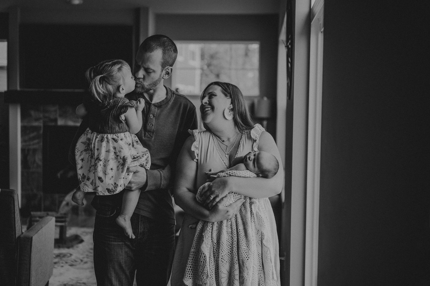 Black and white portrait of family sharing intimate moment by window in home.