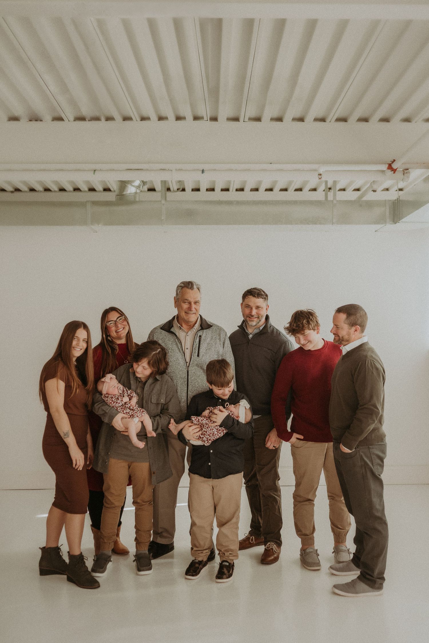 Extended family group photo in casual attire standing together in bright white studio setting.